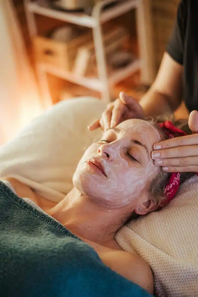 Femme allongé sur une table de soin, avec un soin posé sur le visage et en train de se faire masser.